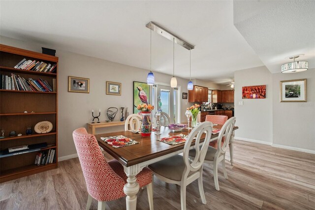 dining area featuring a ceiling fan, light wood-style flooring, and baseboards