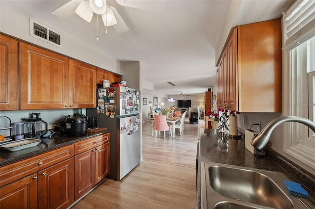 kitchen with brown cabinets, light wood finished floors, visible vents, freestanding refrigerator, and a sink