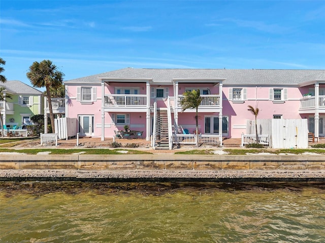 rear view of property featuring stairway, a water view, fence, and stucco siding