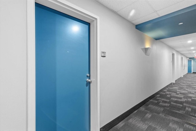 hallway featuring a paneled ceiling, dark carpet, baseboards, and recessed lighting