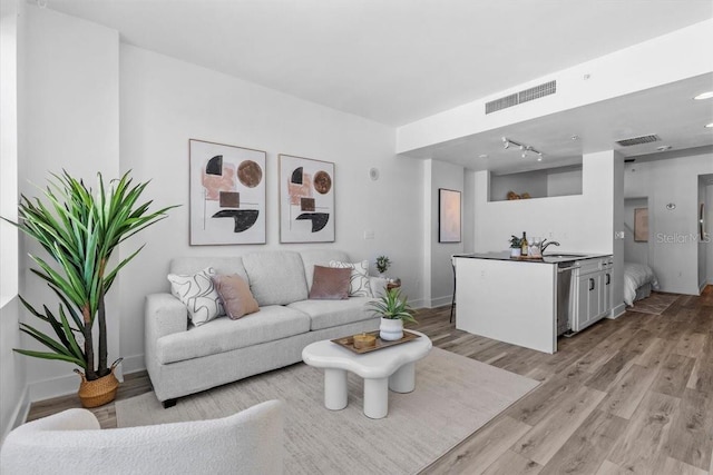 living room with track lighting, visible vents, light wood-style flooring, and baseboards