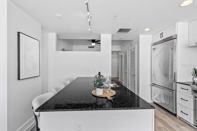 kitchen with light wood finished floors, dark stone countertops, white cabinetry, and stainless steel built in fridge