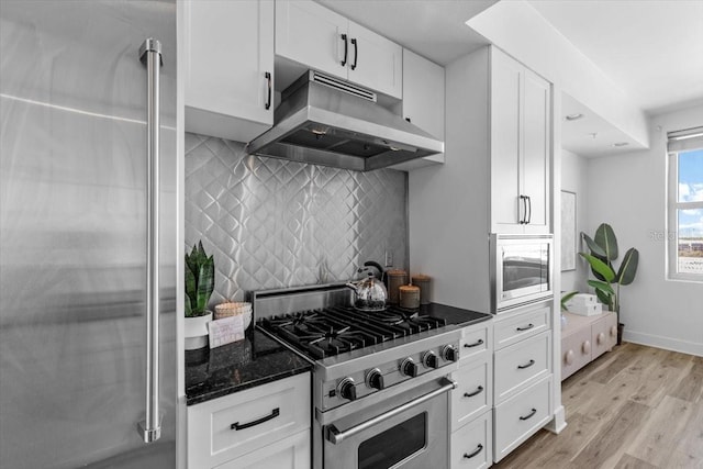 kitchen with premium appliances, under cabinet range hood, white cabinetry, light wood finished floors, and dark stone countertops