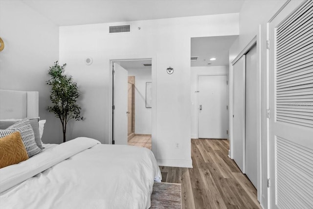 bedroom with light wood-style floors, baseboards, visible vents, and ensuite bathroom