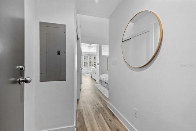 corridor featuring light wood-type flooring, electric panel, and baseboards