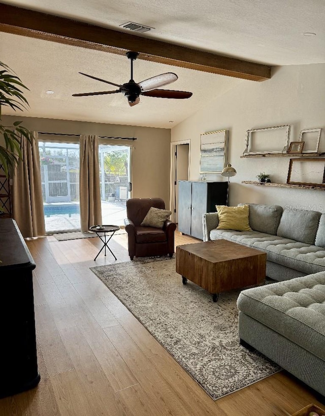 living room with vaulted ceiling with beams, a textured ceiling, visible vents, and wood finished floors