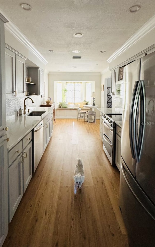 kitchen with light countertops, gray cabinetry, appliances with stainless steel finishes, ornamental molding, and a sink