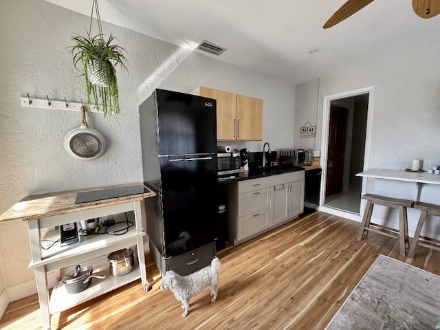 kitchen featuring dark countertops, visible vents, a textured wall, light brown cabinets, and black appliances