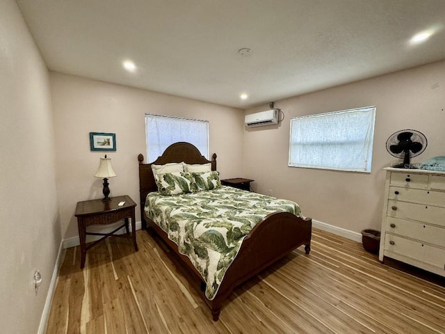 bedroom featuring baseboards, a wall unit AC, light wood finished floors, and multiple windows