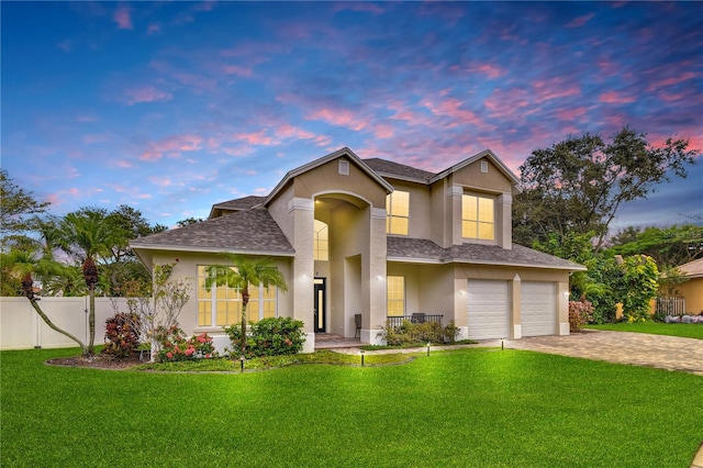 traditional home featuring a garage, fence, a yard, driveway, and stucco siding