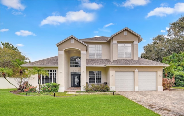 traditional home with a garage, a shingled roof, decorative driveway, a front lawn, and stucco siding