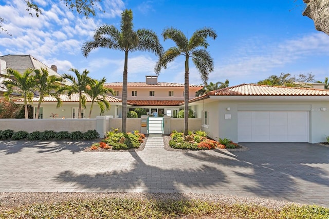 mediterranean / spanish-style home with decorative driveway, a fenced front yard, an attached garage, and stucco siding