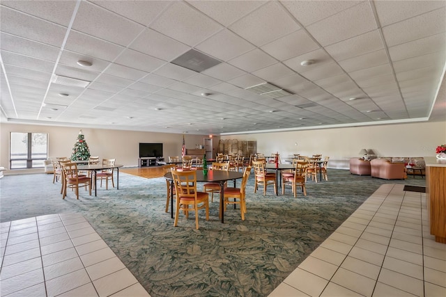 carpeted dining space with a paneled ceiling and tile patterned flooring