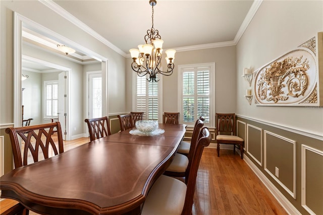 dining area with wainscoting, wood finished floors, crown molding, a chandelier, and a decorative wall