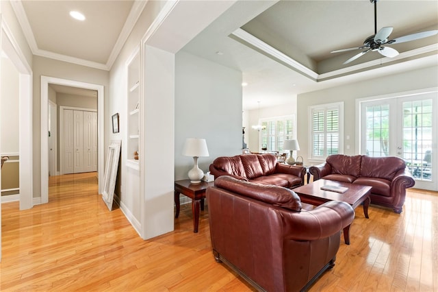 living room featuring light wood finished floors, ornamental molding, a tray ceiling, french doors, and built in shelves