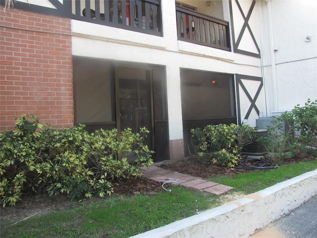 view of exterior entry featuring a balcony, stucco siding, and brick siding