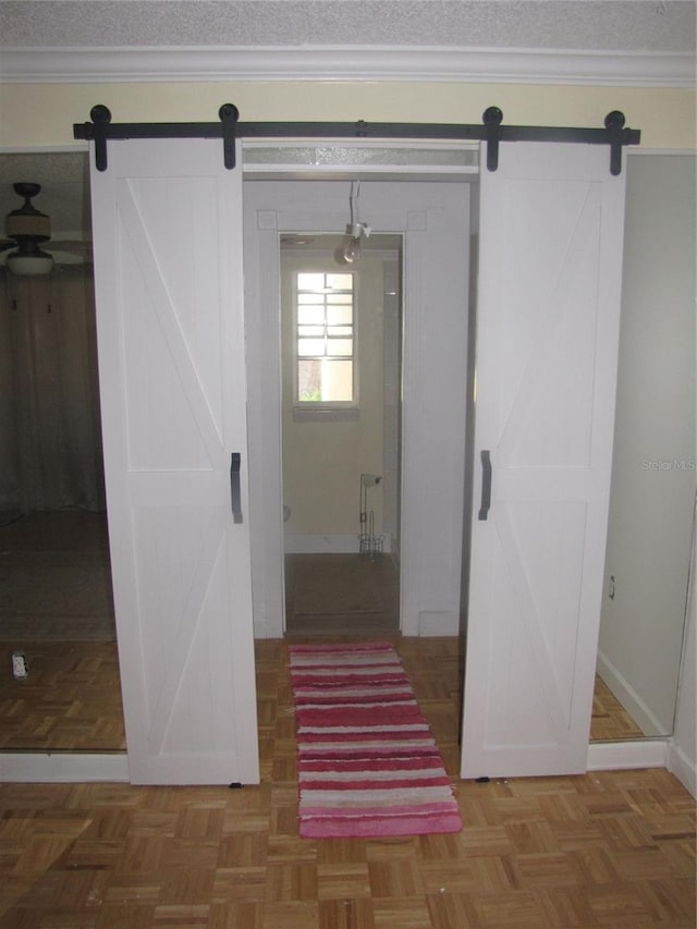 corridor featuring baseboards, a barn door, ornamental molding, and a textured ceiling