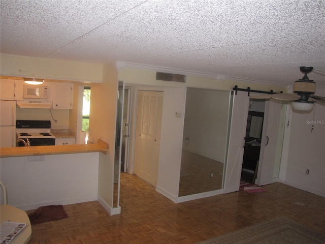 kitchen with electric stove, white microwave, a barn door, a textured ceiling, and under cabinet range hood