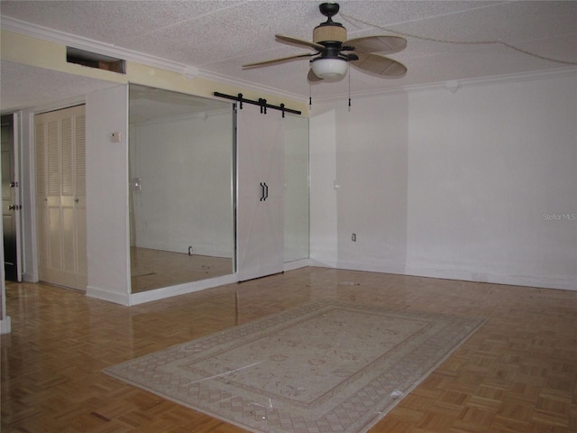 empty room with a barn door, a ceiling fan, a textured ceiling, and ornamental molding