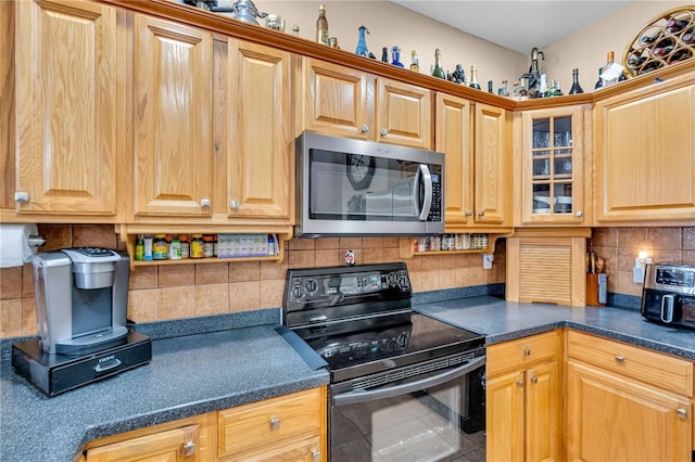 kitchen featuring decorative backsplash, dark countertops, stainless steel microwave, glass insert cabinets, and black range with electric cooktop