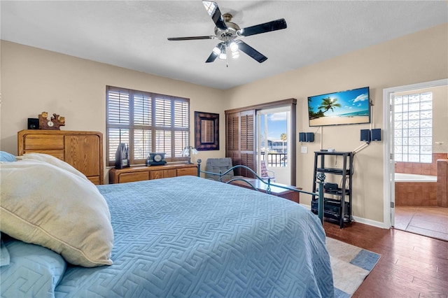 bedroom with ensuite bathroom, dark wood-type flooring, multiple windows, and a ceiling fan