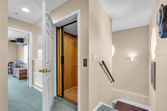 corridor with a textured wall, carpet flooring, and an upstairs landing