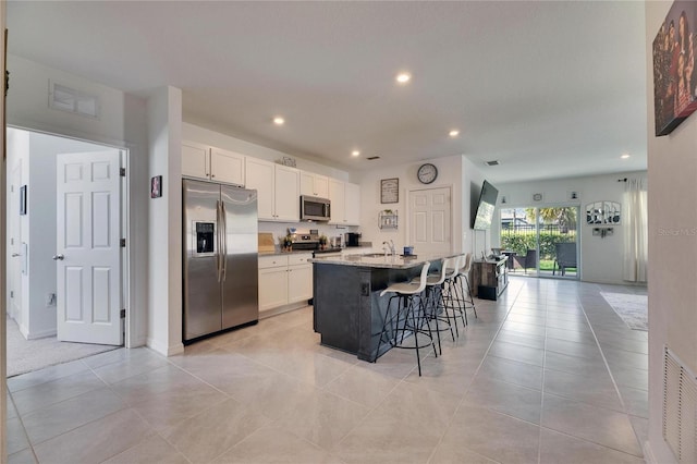 kitchen with an island with sink, a breakfast bar, light stone countertops, stainless steel appliances, and white cabinetry