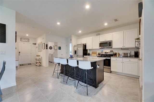 kitchen featuring light stone countertops, a kitchen island with sink, appliances with stainless steel finishes, and white cabinets