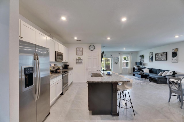 kitchen with open floor plan, stainless steel appliances, a kitchen island with sink, and white cabinets