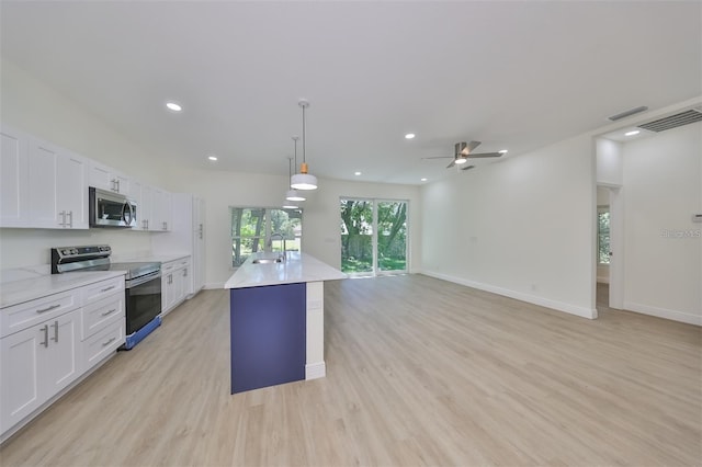 kitchen featuring decorative light fixtures, light countertops, appliances with stainless steel finishes, open floor plan, and white cabinets