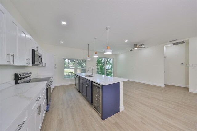 kitchen featuring stainless steel appliances, visible vents, white cabinets, hanging light fixtures, and a center island with sink