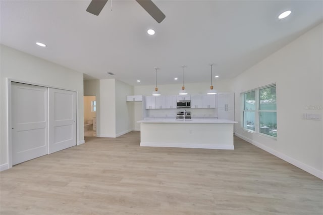 kitchen featuring white cabinets, an island with sink, appliances with stainless steel finishes, light countertops, and pendant lighting