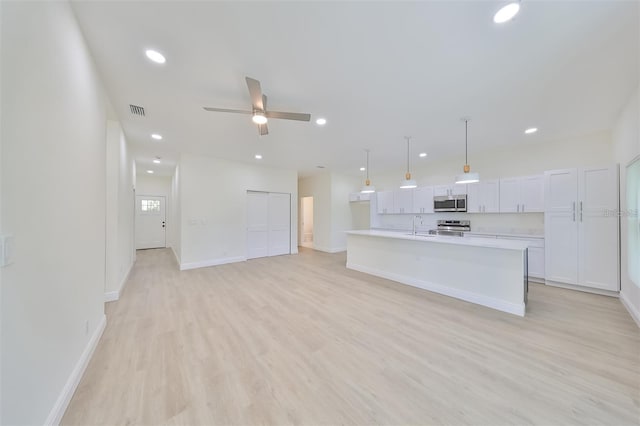 kitchen with a center island with sink, stainless steel appliances, hanging light fixtures, open floor plan, and white cabinets