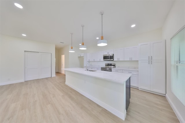 kitchen with an island with sink, appliances with stainless steel finishes, hanging light fixtures, white cabinetry, and a sink