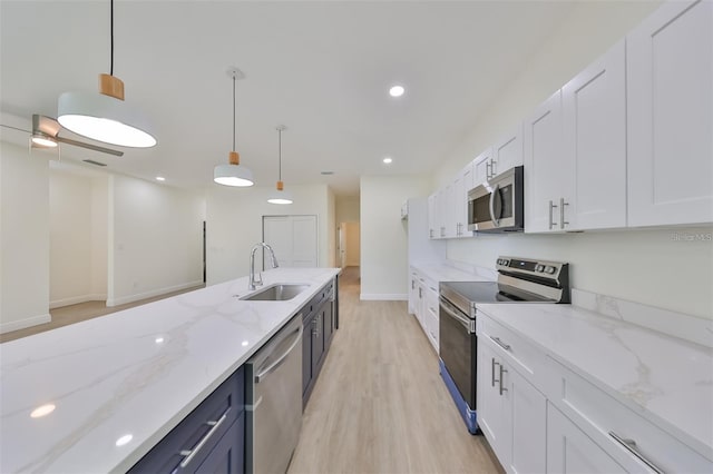 kitchen with stainless steel appliances, a sink, white cabinets, hanging light fixtures, and light stone countertops