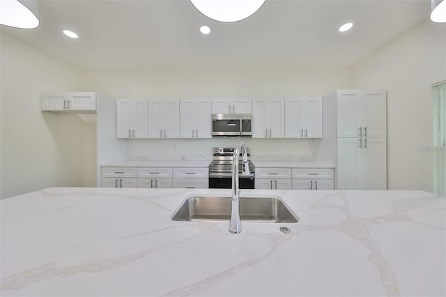 kitchen featuring recessed lighting, appliances with stainless steel finishes, white cabinets, a sink, and light stone countertops