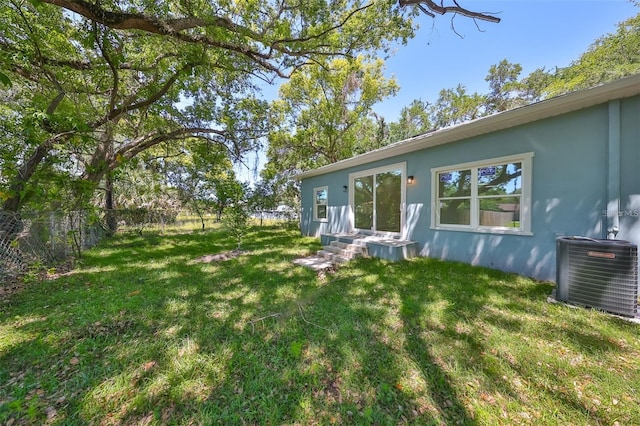 view of yard with entry steps, central AC unit, and fence