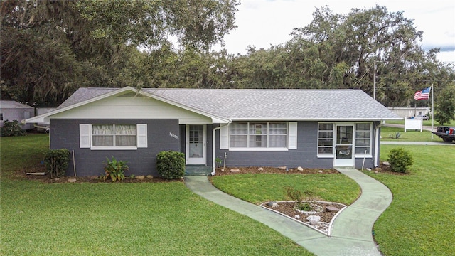 ranch-style home with a shingled roof, concrete block siding, and a front lawn