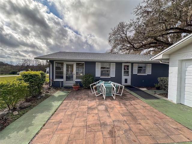 rear view of house with roof with shingles and a patio area