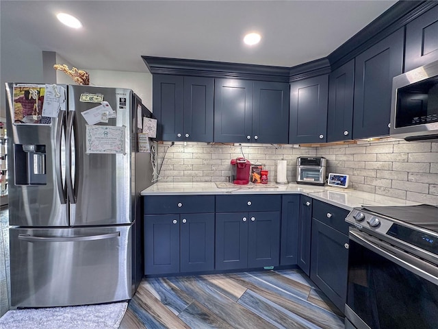 kitchen featuring stainless steel appliances, blue cabinetry, light stone countertops, and decorative backsplash