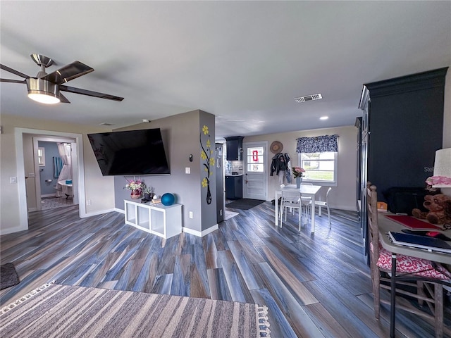 living area with dark wood-style floors, ceiling fan, visible vents, and baseboards