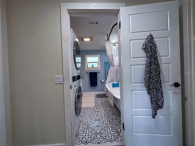 full bathroom with a tub to relax in, stacked washer / dryer, visible vents, baseboards, and tile patterned floors