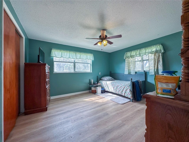 bedroom featuring a closet, light wood-style flooring, a ceiling fan, a textured ceiling, and baseboards