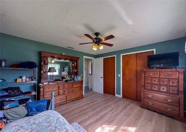 bedroom featuring visible vents, ceiling fan, a textured ceiling, light wood-type flooring, and two closets