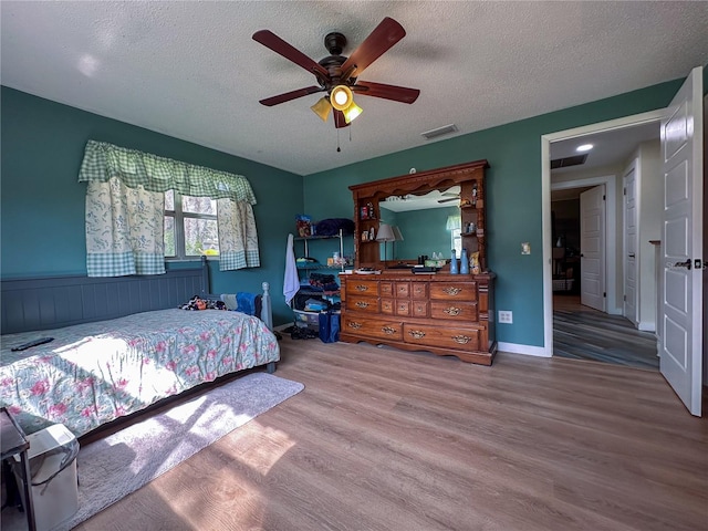 bedroom featuring ceiling fan, a textured ceiling, visible vents, and wood finished floors