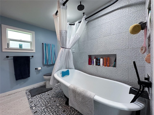 bathroom featuring a soaking tub, baseboards, a tile shower, and toilet