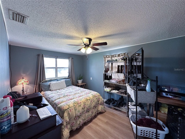 bedroom featuring a ceiling fan, visible vents, a textured ceiling, and wood finished floors