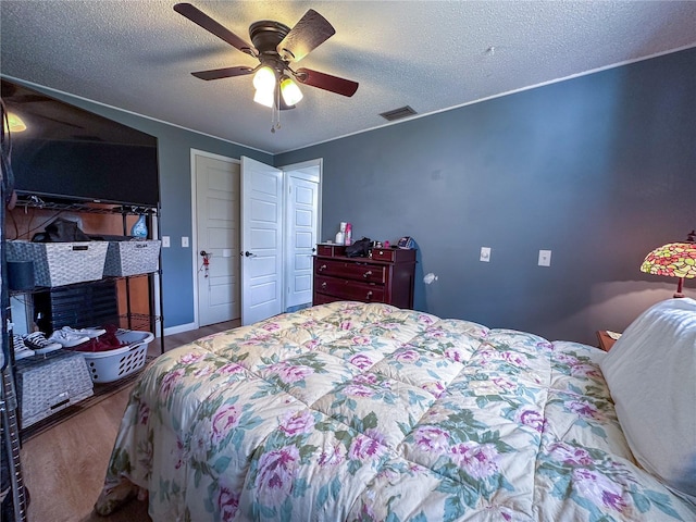 bedroom with a textured ceiling, ceiling fan, wood finished floors, and visible vents