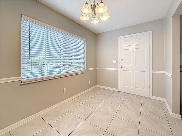 empty room featuring baseboards, a notable chandelier, and light tile patterned flooring