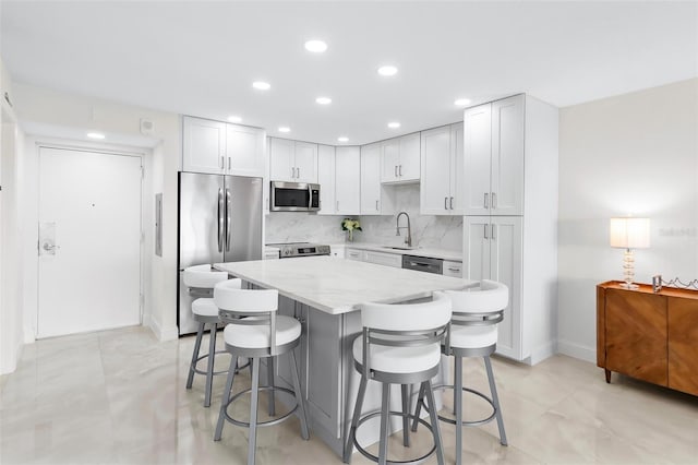 kitchen with a breakfast bar, a sink, appliances with stainless steel finishes, backsplash, and light stone countertops